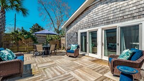 Una terraza con mobiliario exterior, una mesa cubierta y un ventanal corredera que da a una habitación.