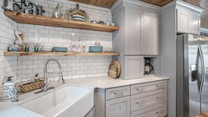 Una cocina moderna con armarios blancos, estantes de madera y un refrigerador de acero inoxidable.
