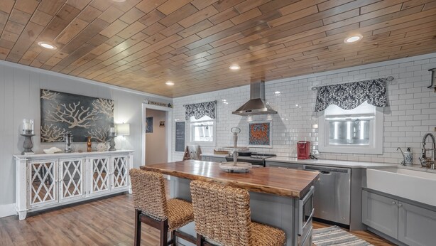 Una cocina moderna con techo de madera, salpicadero de azulejos blancos y una isla central con taburetes de bar.