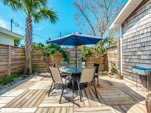 Une terrasse en bois avec une table et des chaises, placée sous un parasol bleu, et entourée d’une clôture en bois et d’arbres.