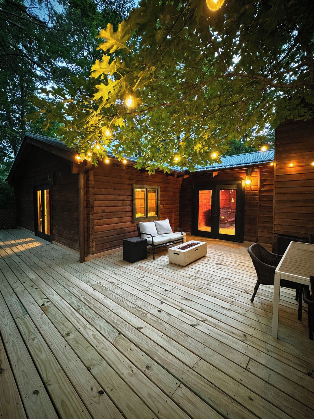 A wooden deck with a sofa, a table, and a fireplace.
