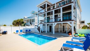 A modern multi-story building with a swimming pool and lounge chairs. - Golden Hour: Luxurious Home with Pool Overlooking Lockwood Folly Inlet (Oak Island)