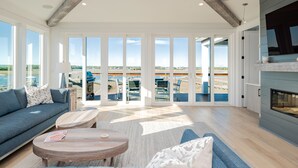 A spacious living room with a large window, a sofa, a coffee table, and a fireplace. - Golden Hour: Luxurious Home with Pool Overlooking Lockwood Folly Inlet (Oak Island)