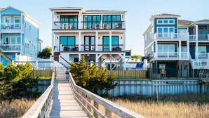 A multi-story beachfront property with a wooden boardwalk leading to the entrance. - Golden Hour: Luxurious Home with Pool Overlooking Lockwood Folly Inlet (Oak Island)