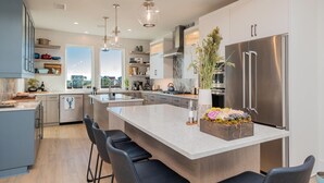 A modern kitchen with a large island, stainless steel appliances, and bar stools. - Golden Hour: Luxurious Home with Pool Overlooking Lockwood Folly Inlet (Oak Island)