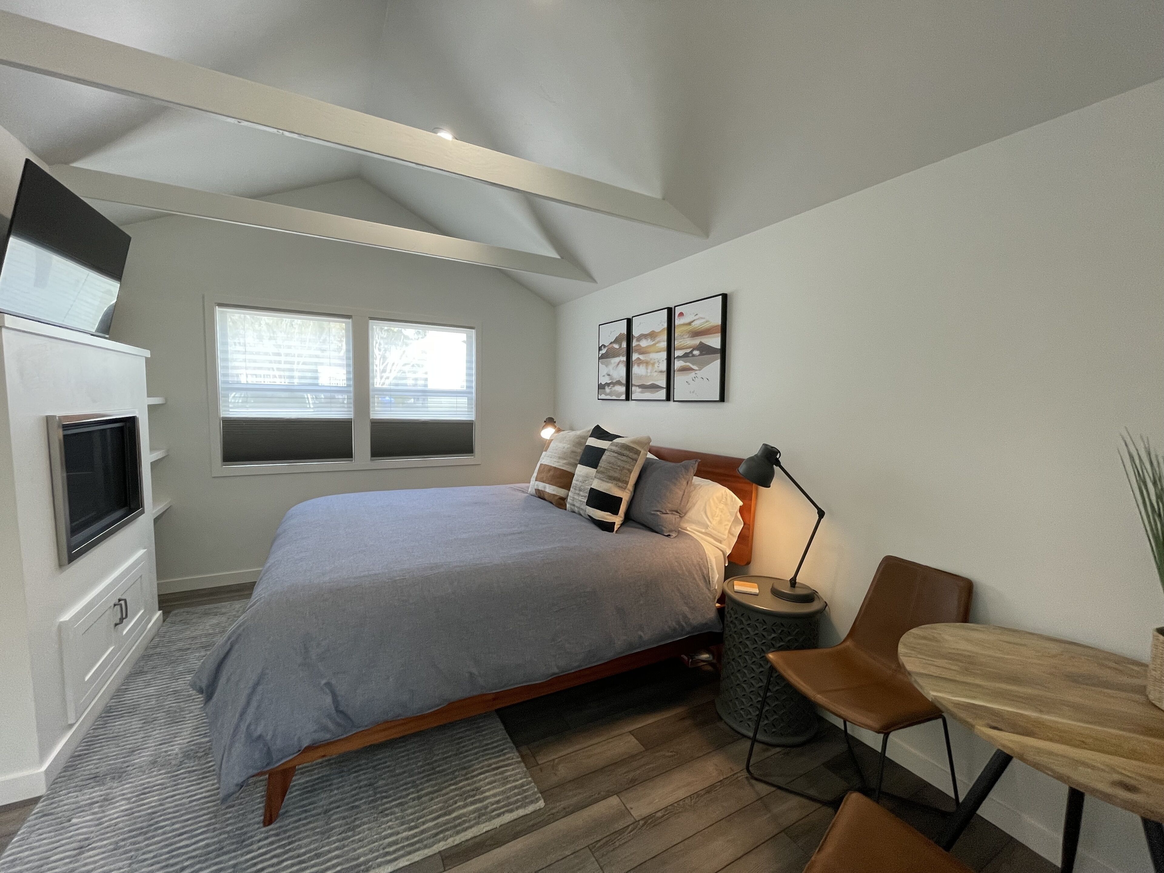 A modern bedroom with a bed, bedside table, lamp, and a small wooden table.