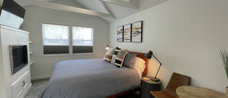A modern bedroom with a bed, bedside table, lamp, and a small wooden table.