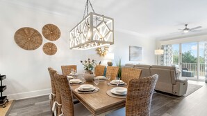 Un coin repas avec une table en bois dressée pour six personnes, entourée de chaises en osier, d’un luminaire suspendu et de trois assiettes décoratives fixées au mur.