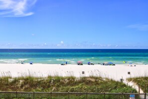 A beach with clear blue water, a sandy shore, and a few beach umbrellas.