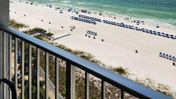 A beach view from a balcony with a railing, clear sky, and ocean.