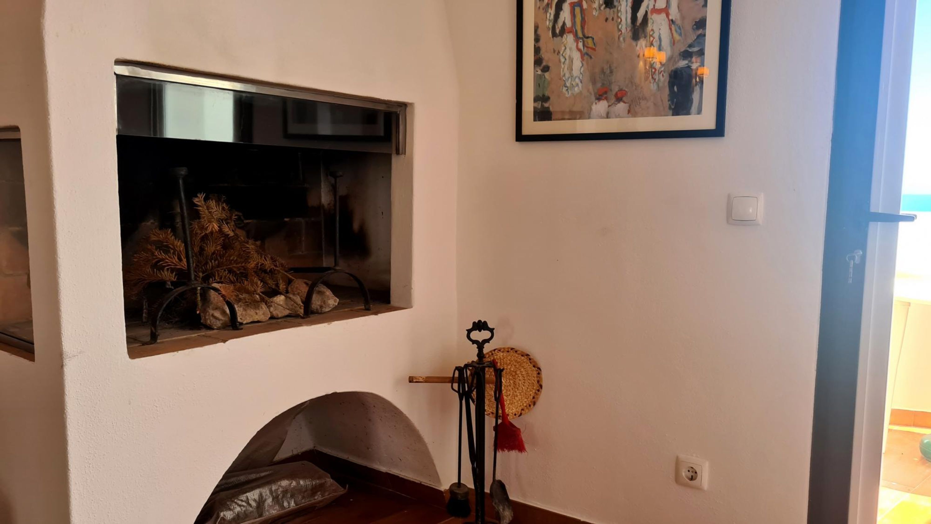 Quarto com lareira, quadro abstrato emoldurado e janela decorada com ramos de pinheiro.