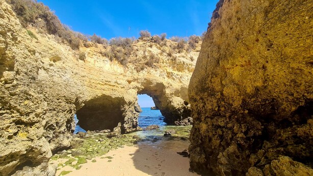 Formação rochosa natural com entrada de caverna que dá para uma praia.