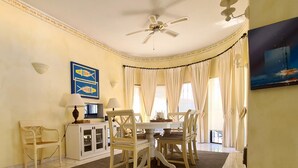 Uma sala de jantar com mesa e cadeiras, um ventilador de teto e um quadro na parede.
