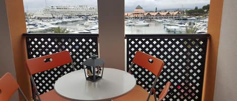 Un balcón con mesa y sillas, con vista a un puerto deportivo con barcos y edificios.