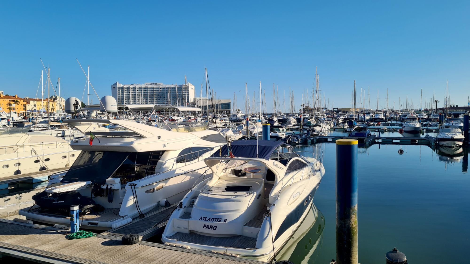Una marina con diversi yacht ormeggiati, un grande edificio sullo sfondo e acqua calma.