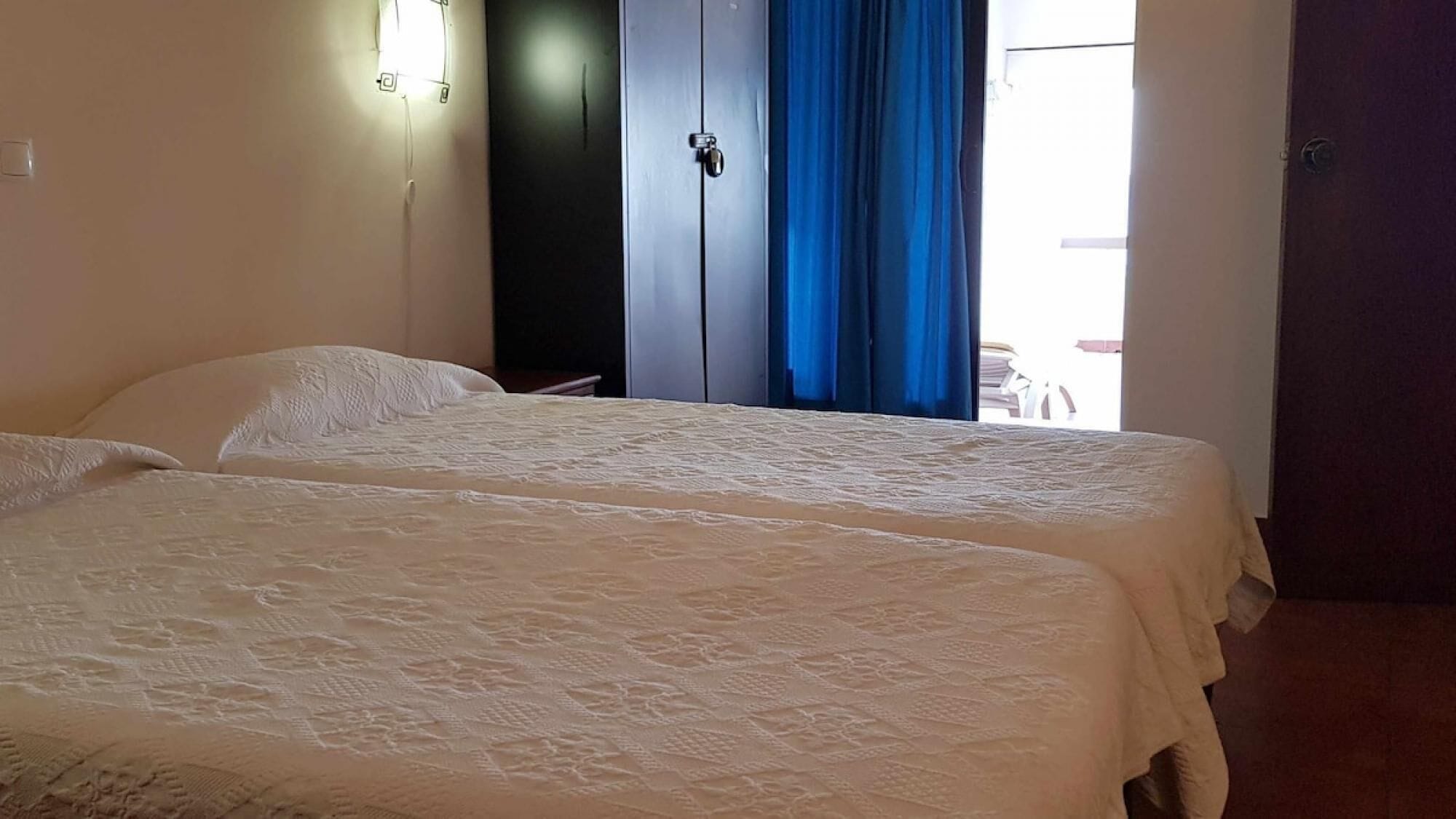 A room with two beds, a wardrobe, and a door.