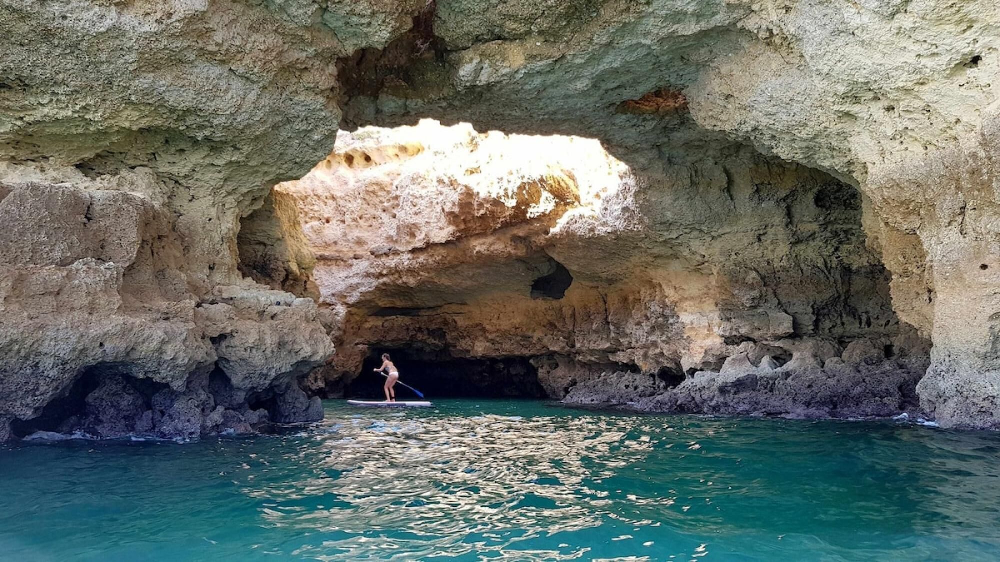 A person on a paddleboard in a natural rock formation with clear water.