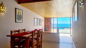 Ein Essbereich mit einem Holztisch und Stühlen, einem Fernseher und Blick aufs Meer.