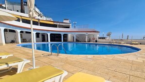 Bereich mit Pool, Liegestühlen und einem Rettungsring auf dem Deck eines Kreuzfahrtschiffs.