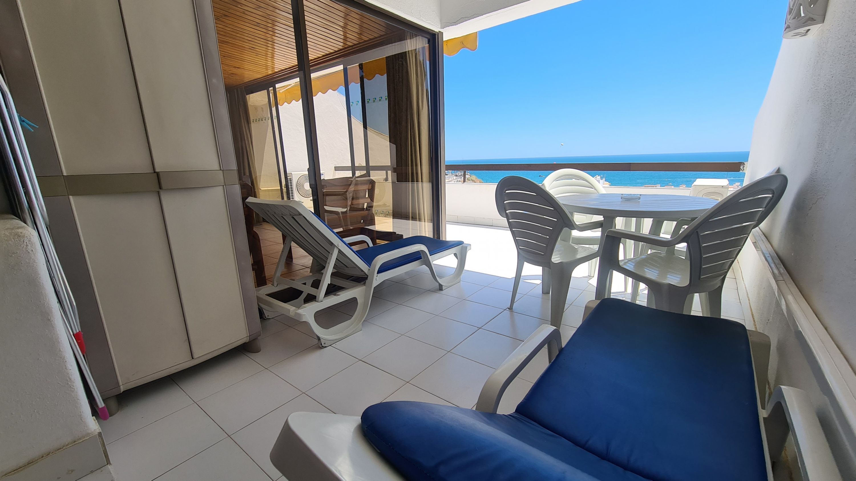 Een balkon met uitzicht op zee, een tafel met stoelen en een ligstoel.