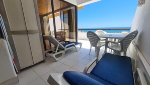 Un balcón con vistas al mar, una mesa con sillas y una tumbona.