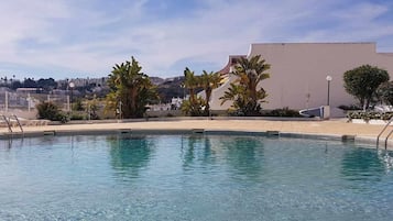 Una piscina con agua cristalina, rodeada de palmeras y un edificio al fondo.