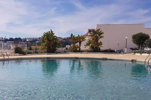 A swimming pool with clear water, surrounded by palm trees and a building in the background.
