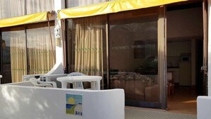 Une chambre d’hôtel avec une porte-fenêtre coulissante, un petit balcon avec une table et des chaises, et un auvent jaune.