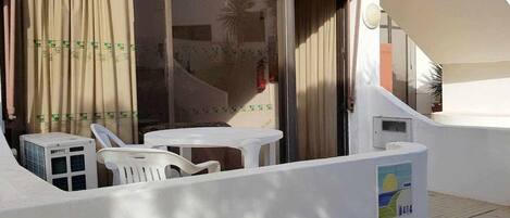 A balcony with a white table and chairs, a yellow awning, and a white wall with a number sign.