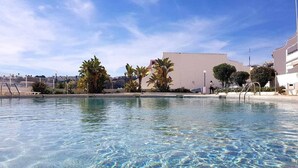 Une piscine aux eaux cristallines, avec en arrière-plan des bâtiments et des arbres.