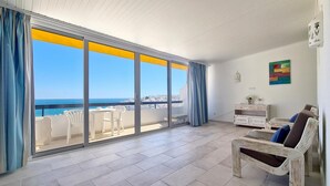 Un balcon spacieux offrant une vue dégagée sur la mer et le paysage urbain, aménagé avec des chaises blanches et un meuble blanc.