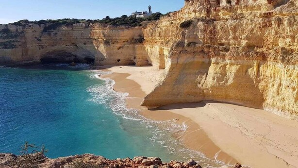Un paysage côtier caractérisé par des falaises, une plage de sable et des eaux d’un bleu limpide.