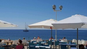 Un café situé en bord de mer, avec une terrasse, des parasols et une vue sur l’océan.