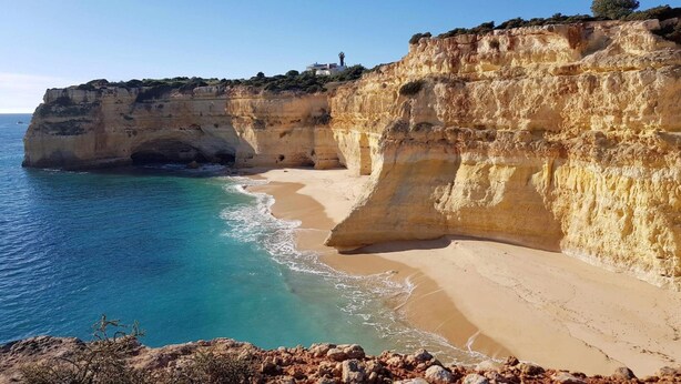 Un paysage côtier avec une plage de sable, une falaise et un phare en arrière-plan.