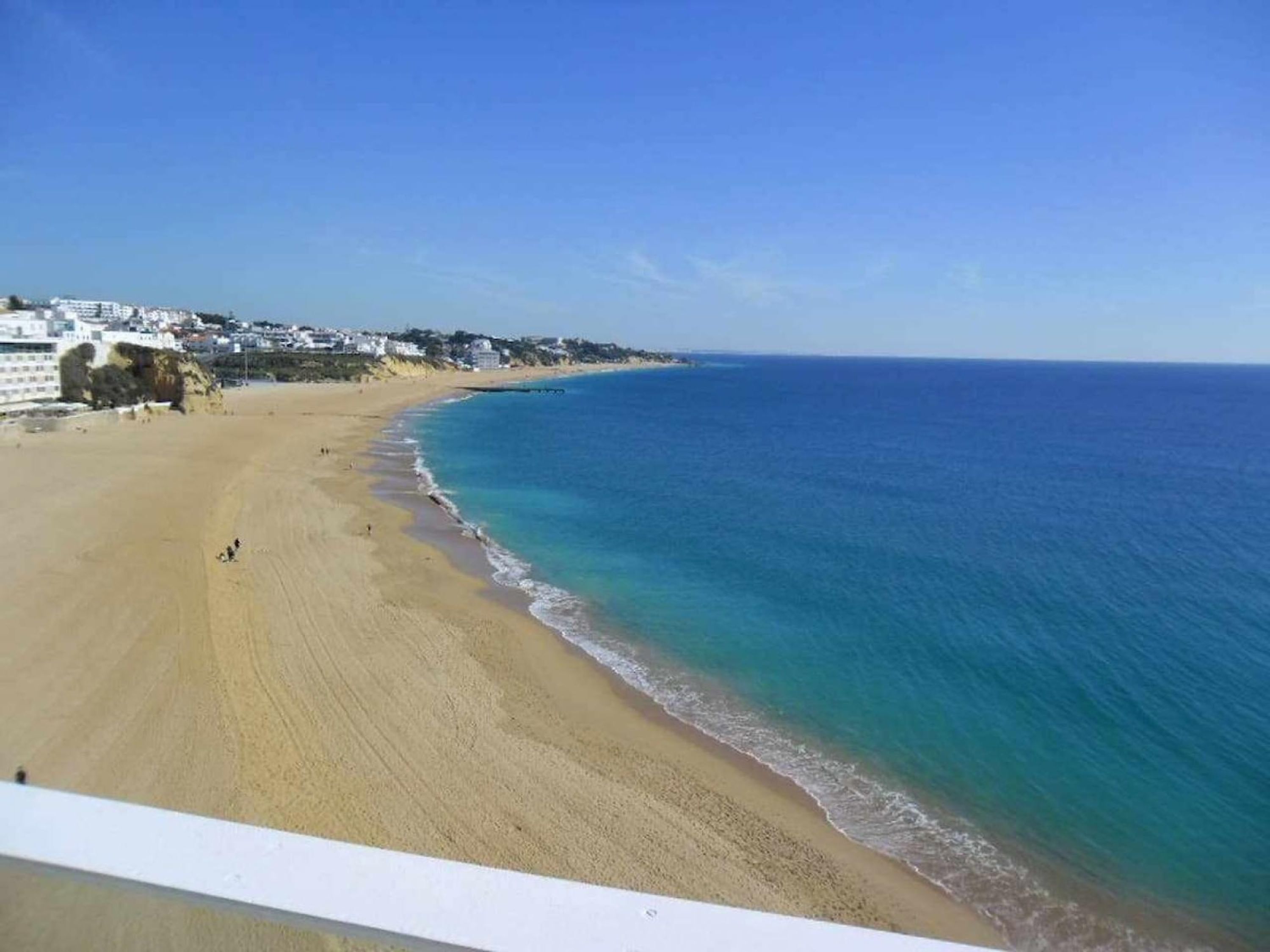 Une plage avec une eau d’un bleu limpide, un rivage sablonneux et des bâtiments en arrière-plan.
