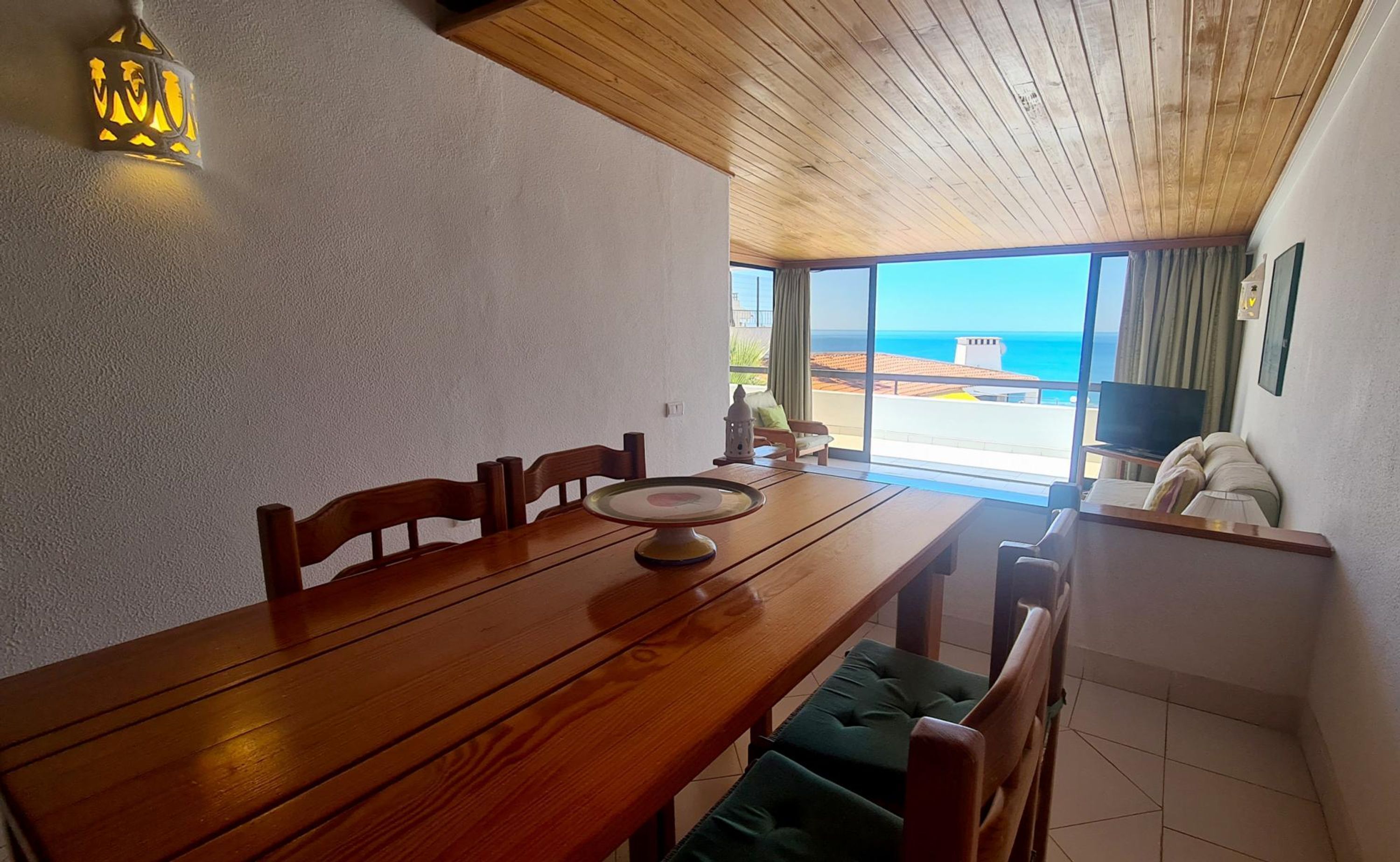 Un comedor con una mesa de madera, sillas y vista al mar a través de amplios ventanales.