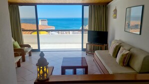 Un soggiorno con divano, televisore, tavolo e vista sul mare.