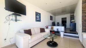 A modern living room with a white sofa, a glass coffee table, and a flat-screen TV mounted on the wall. - Albufeira Sea View 25 (Albufeira)