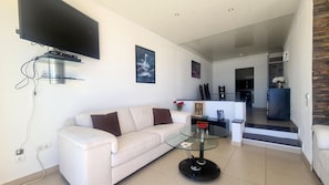 A modern living room with a white sofa, a glass coffee table, and a flat-screen TV mounted on the wall.