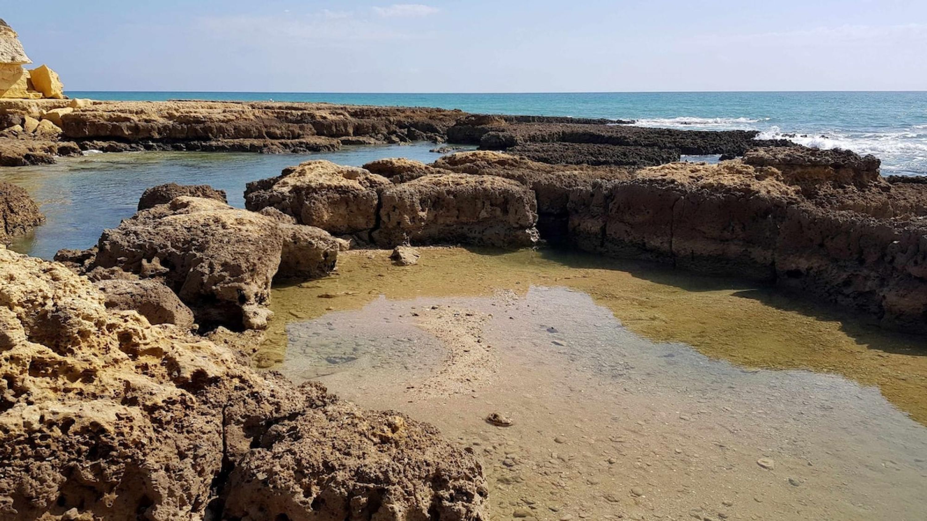 A rocky coastal landscape with clear water and a sandy beach.