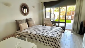 Ein Schlafzimmer mit einem Bett, Kissen, einem Sessel, einem Tisch mit Gläsern und Blick ins Freie.