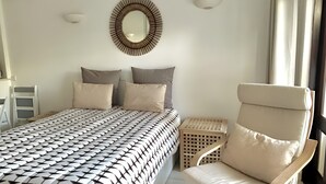Ein Schlafzimmer mit einem Bett, Kissen, einem Sessel, einem kleinen Tisch und einem Wandspiegel.