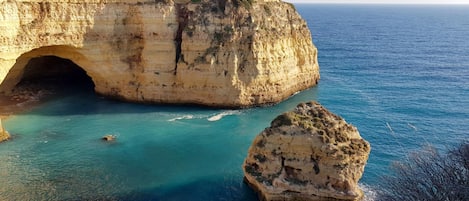 Um penhasco costeiro com uma abertura natural de caverna e águas turquesa cristalinas.