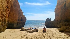 A beach with large rock formations on either side, a clear sky, and a boat in the distance. - Albufeira Balaia Mar e Sol (Albufeira)
