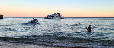 A boat on calm waters with a rocky coastline in the background.