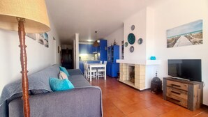 A living room with a sofa, TV, and fireplace. There is a kitchen in the background with blue cabinets and a dining area. - Albufeira Balaia Mar e Sol (Albufeira)