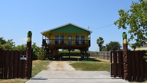 A two-story house with a balcony, a wooden fence, and a clear sky. - Pineapple House - Fishing Paradise! Gated, Pet Friendly, Secluded (Port Bolivar)