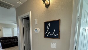 A hallway with a light fixture, a door, and a wall-mounted sign. - Pineapple House - Fishing Paradise! Gated, Pet Friendly, Secluded (Port Bolivar)