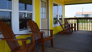 A porch with wooden chairs and a rocking chair, a yellow exterior wall, and a door with a sign. - Pineapple House - Fishing Paradise! Gated, Pet Friendly, Secluded (Port Bolivar)