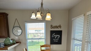 A dining area with a wooden table and chairs, a chandelier, a clock, and a window with blinds. - Pineapple House - Fishing Paradise! Gated, Pet Friendly, Secluded (Port Bolivar)